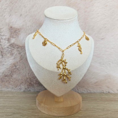 Vooraanzicht van een gouden koraalketting met maritieme bedels op display tegen een neutrale achtergrond.
