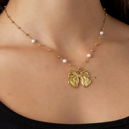 Goudkleurige parelketting met elegante strikhanger en subtiele pareldetails - om de hals gedragen